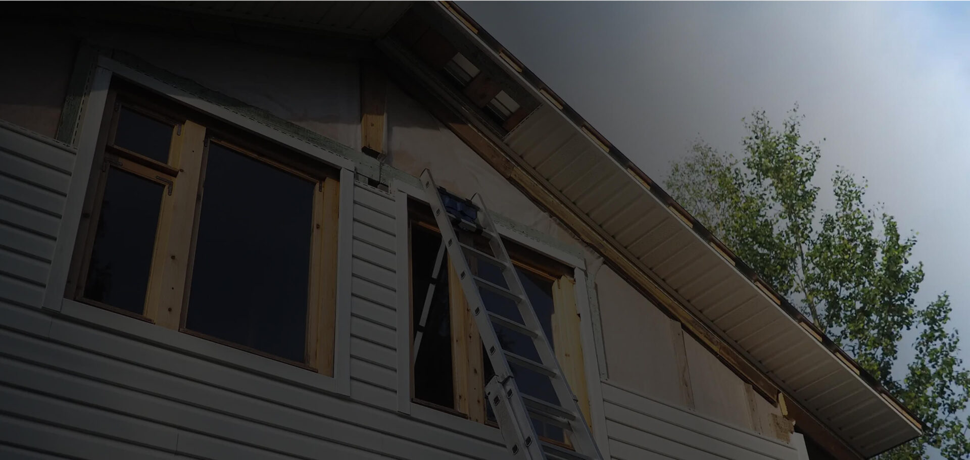 Home exterior during siding replacement with exposed window framing and ladder, showing preparation for moisture protection and leak-resistant siding installation