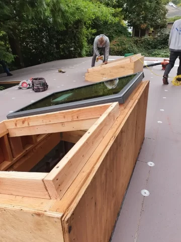 Contractor assembling a skylight curb and installing a new skylight on a flat roof, demonstrating RainWise leak-proof skylight installation and waterproofing in Portland