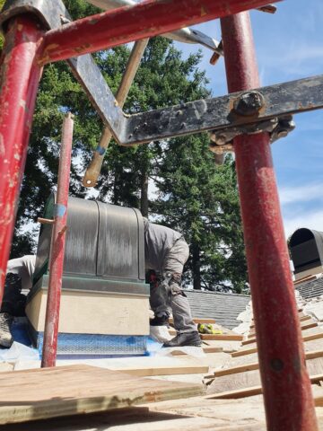Technician repairing and waterproofing a chimney while standing on scaffold during exterior restoration