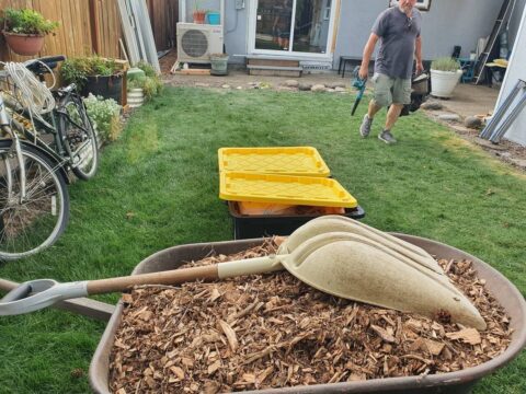 Wheelbarrow with wood mulch and tools on a residential backyard jobsite during exterior repair work in Portland