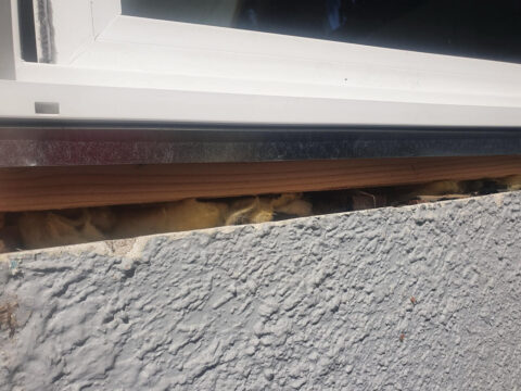 Close-up of a window installed with an exposed gap under the frame, showing missing flashing and insulation that can lead to water intrusion and leaks